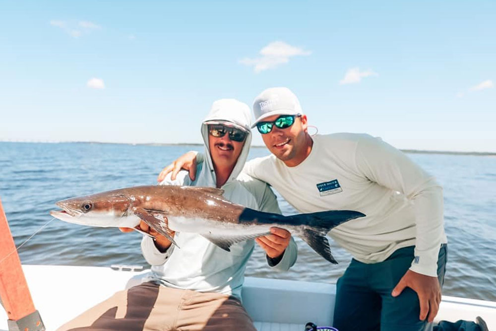 Image of two men holding fish, featuring Saltwater Fishing Charters and highlighting their charter services, showcasing a successful fishing trip.